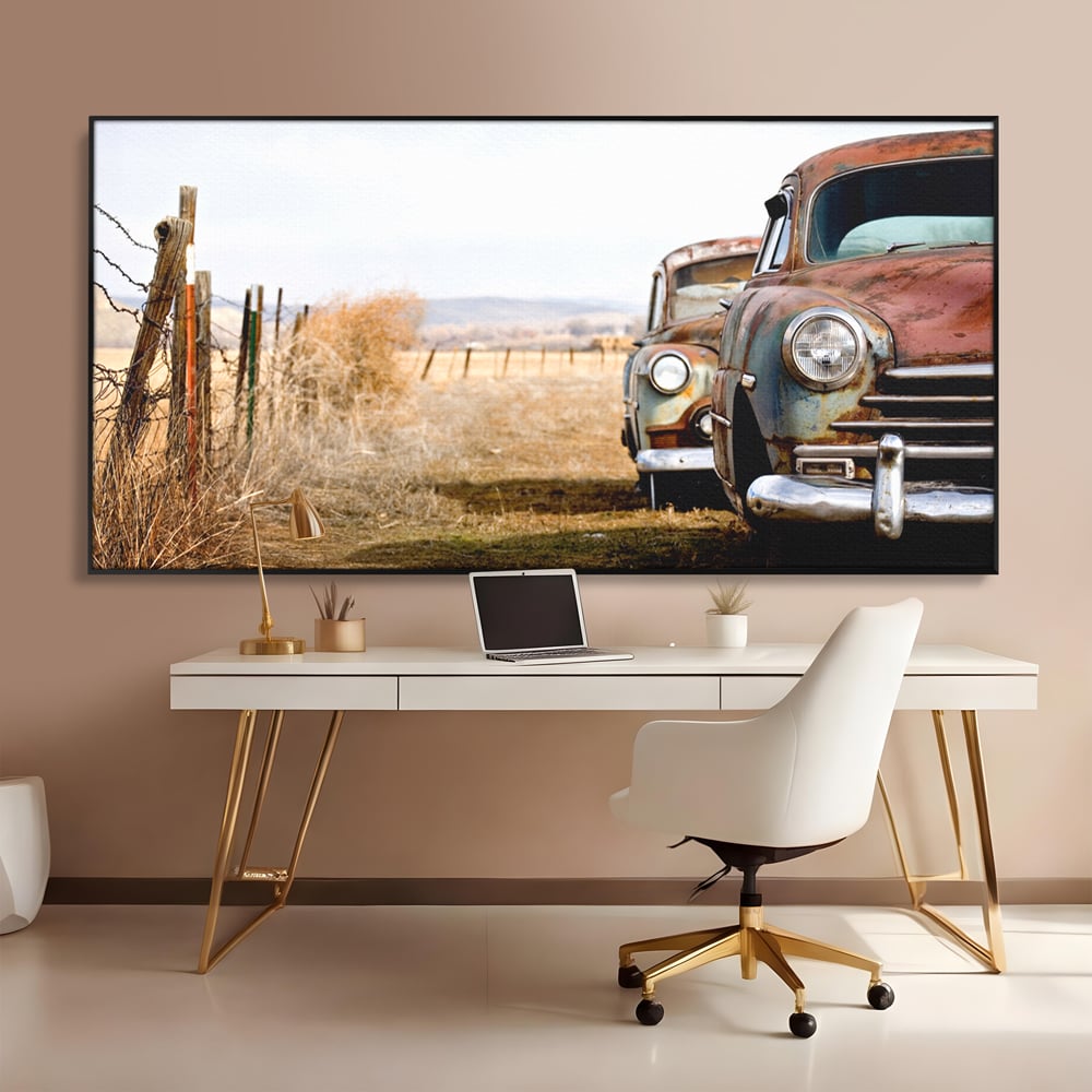 Tablou canvas cu doua masini ruginite pe un camp uscat, in rama de aluminiu negru, pe perete intr-un birou